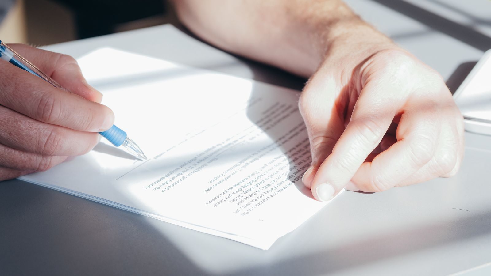 Close-up of a hand signing a printed document with a blue pen