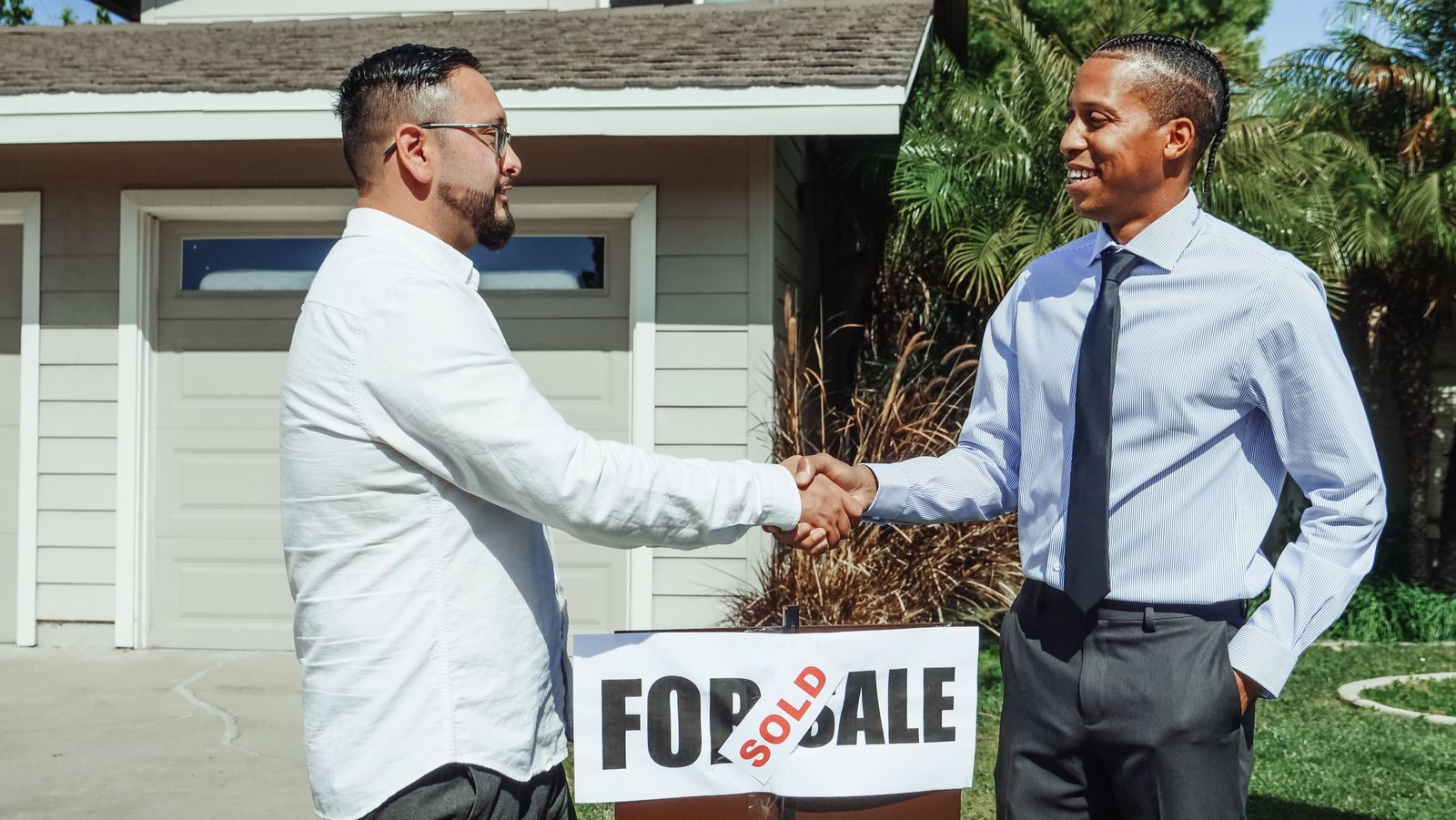 Two men shaking hands in front of a house beside a For Sale sign marked Sold, a deal made to sell your house fast