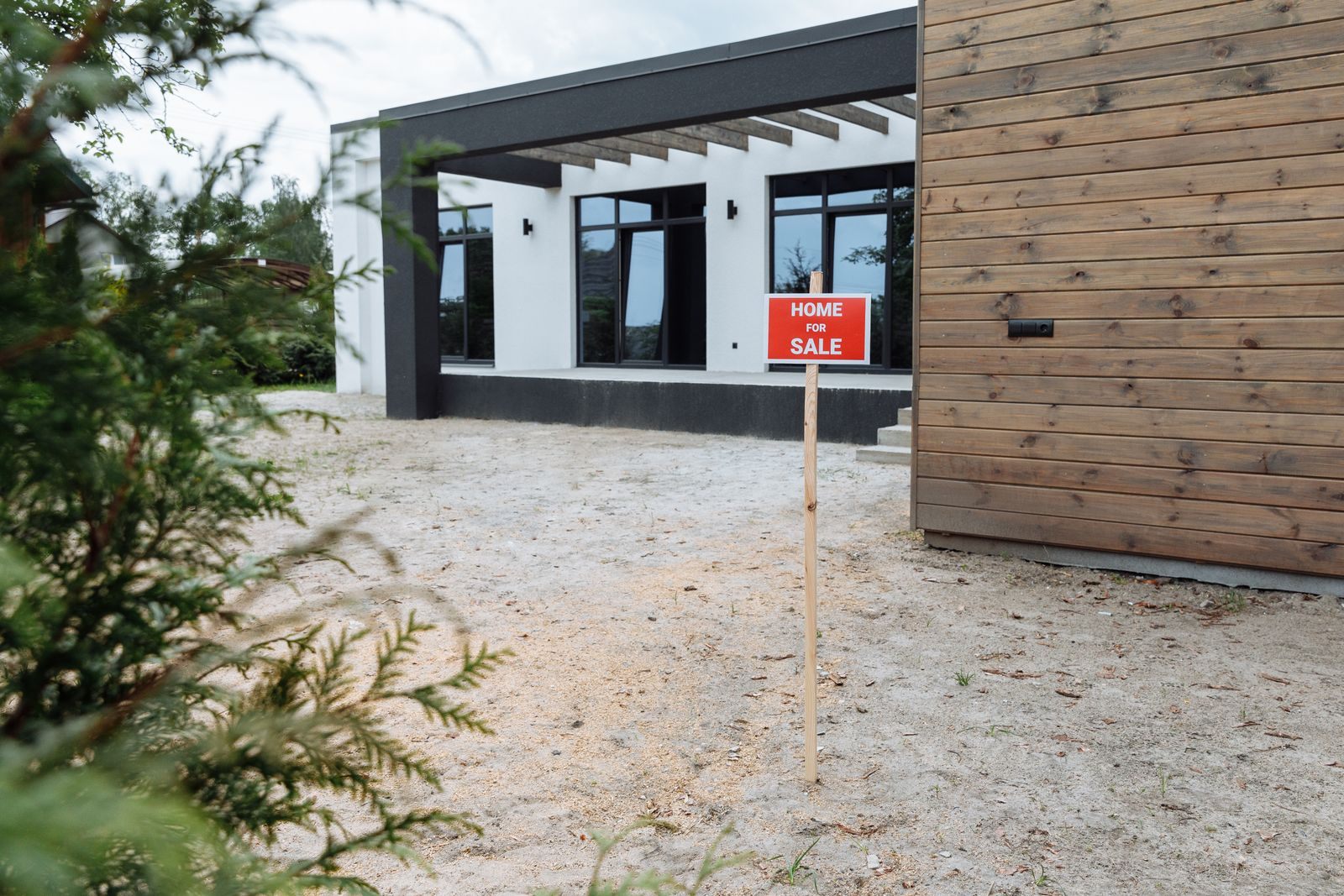 Modern house with wood siding and a small Home For Sale sign in the yard, a home listed to sell without a realtor