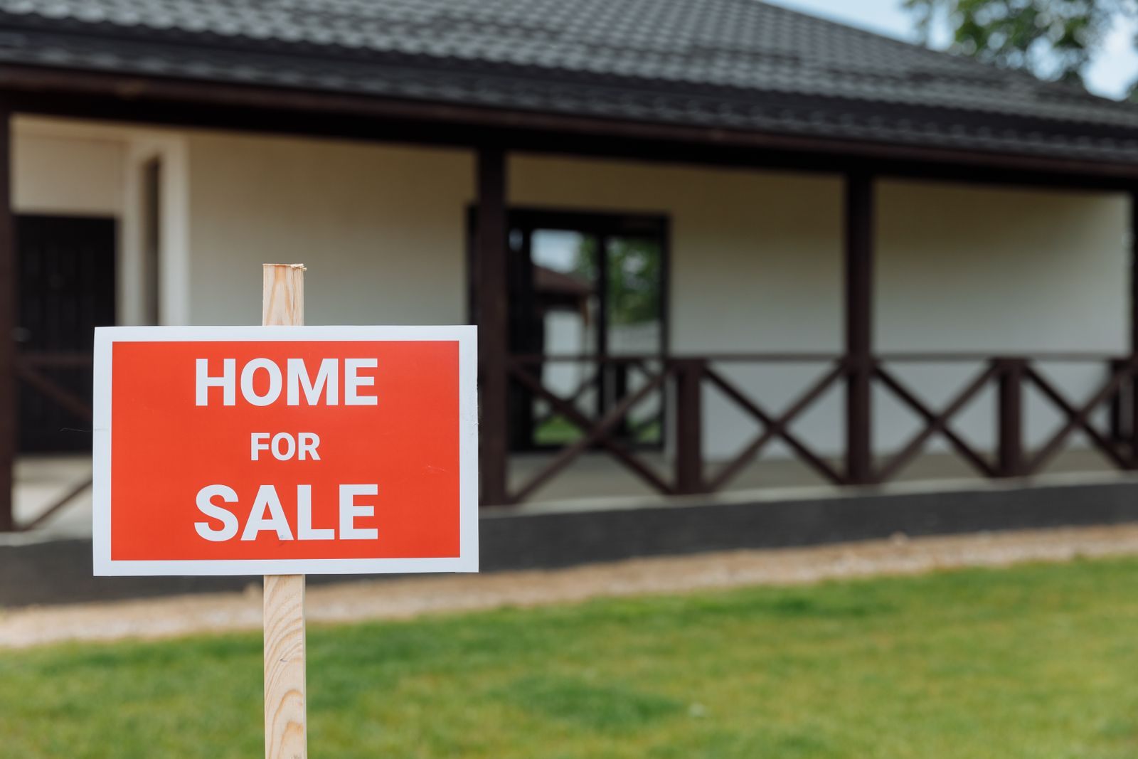 Red Home For Sale sign on the lawn of a house with a covered porch, the first step in how to sell your house