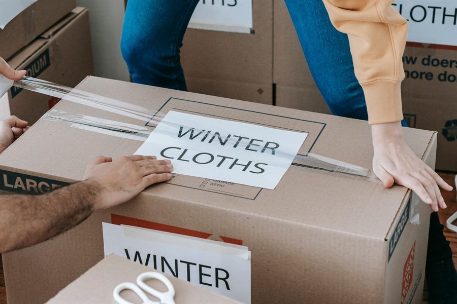Hands taping a moving box labeled Winter Clothes