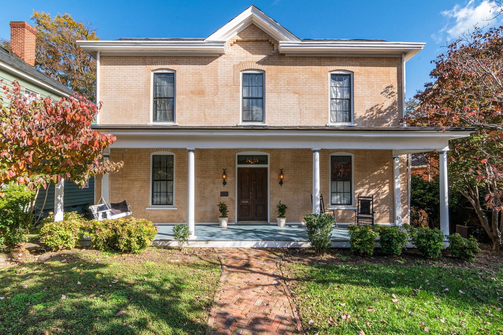 Two-story brick house with a white front porch, autumn trees and a neat front lawn