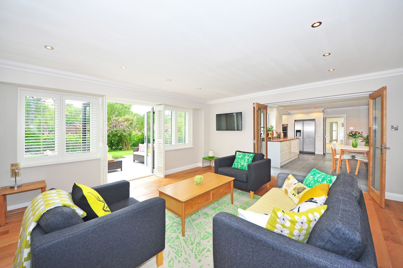 Bright, tidy living room with gray sofas, yellow cushions and an open view to the kitchen
